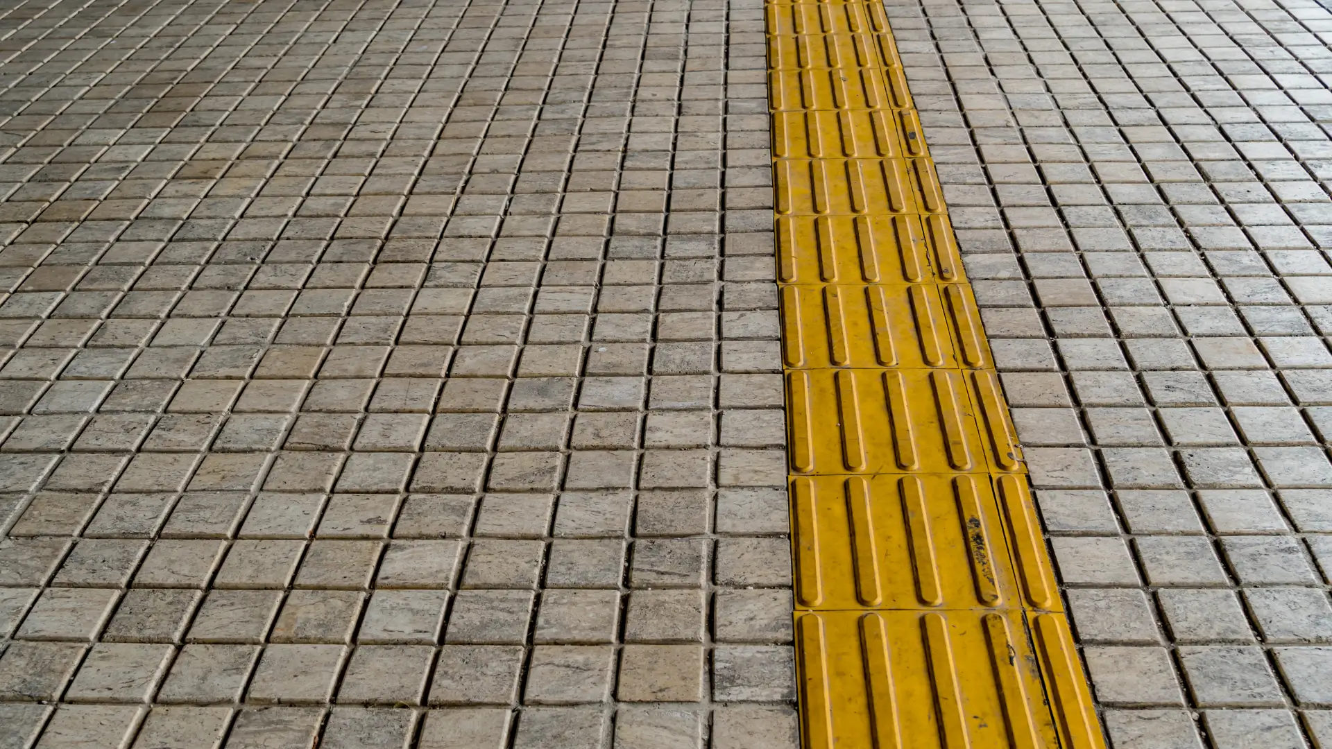 Paved metro platform floor with a yellow safety line running along the edge, evoking guidance markers designed for everyone's safety