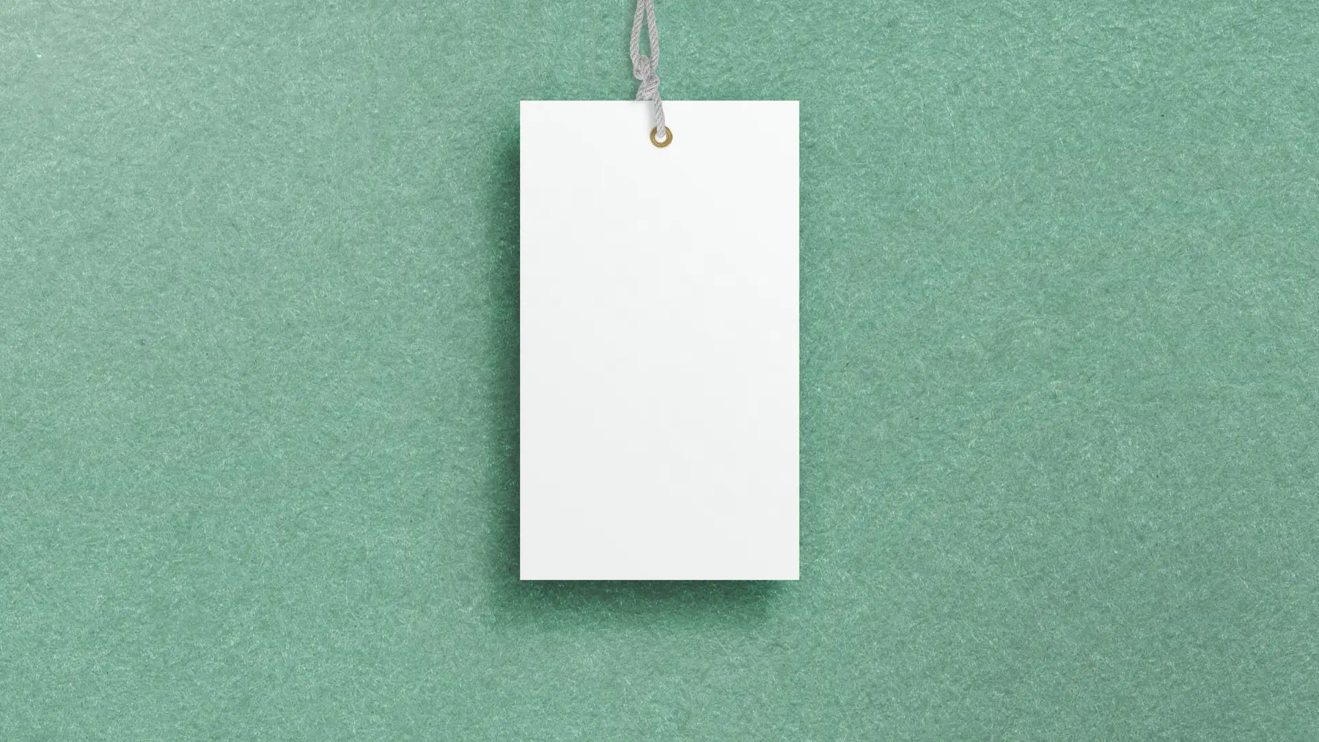 Blank white price tag hanging from a grey string by a brass eyelet, against textured sea-green paper